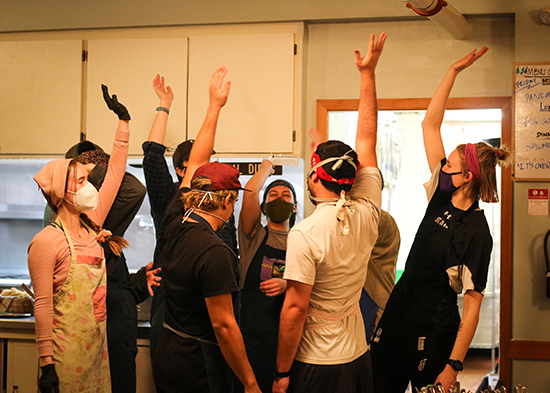 A group of eight cooks raise their hands after a huddle in the kitchen