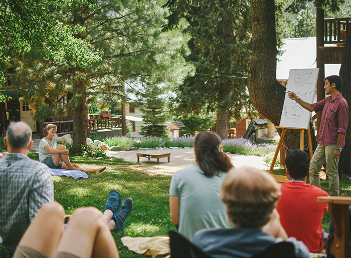 Outdoor class with instructor pointing to whiteboard and people sitting on grass