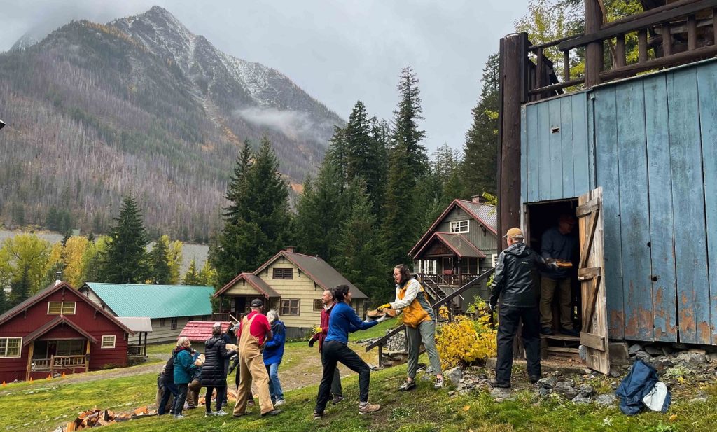 A crowd of people pass firewood to each other with houses and a mountain in the background